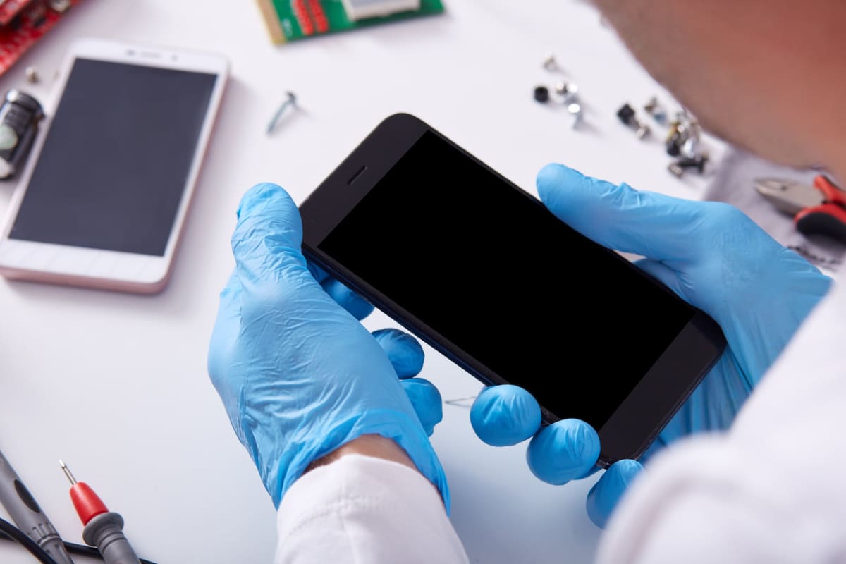A technician in protective gloves examining a smartphone with a blank screen